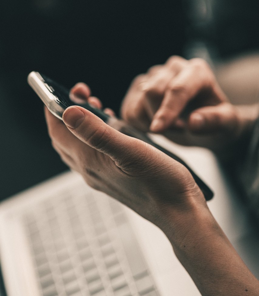 Hænder med telefon og computer i baggrunden